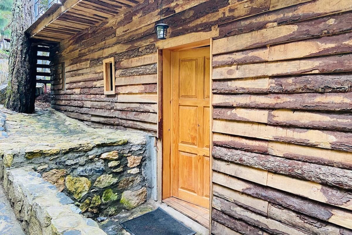 A rustic log cabin with a wooden door, stone steps, and a lantern above the door.