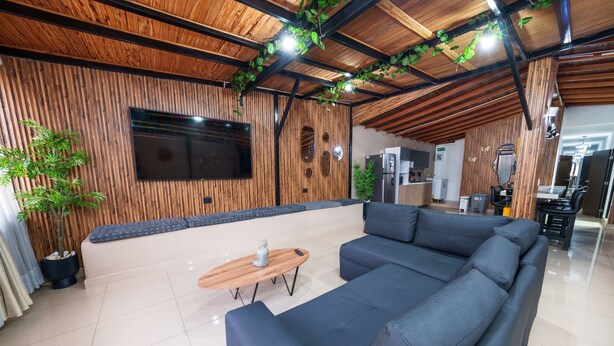 A modern living area with a sectional sofa, a wooden coffee table, and a flat-screen TV mounted on a wooden wall.
