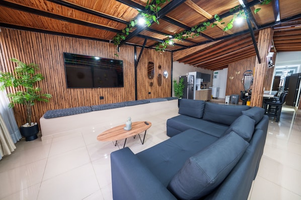 A modern living area with a sectional sofa, a wooden coffee table, and a flat-screen TV mounted on a wooden wall.