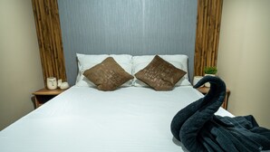 A bed with white bedding, two brown pillows, a dark blue towel, and a wooden nightstand with a small plant and a white container.