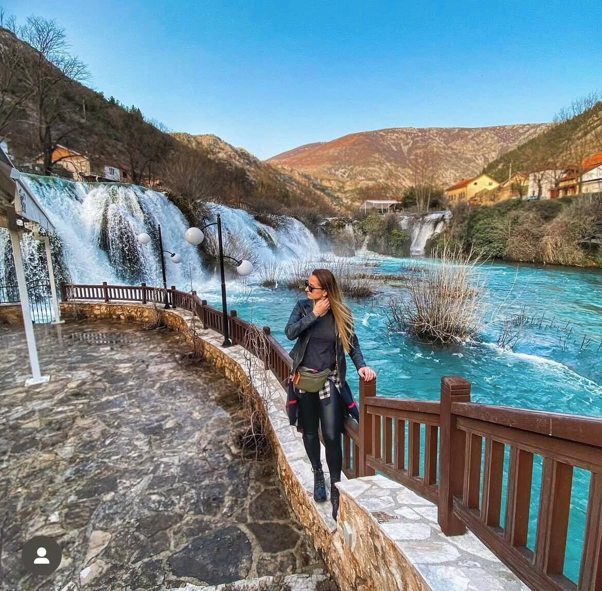 Un sendero de piedra que conduce a una baranda de madera con vistas a un río y una cascada.