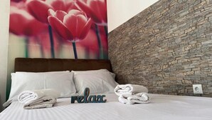 A neatly made bed with white linens, a 'relax' sign, and towels on a wall with a stone pattern.
