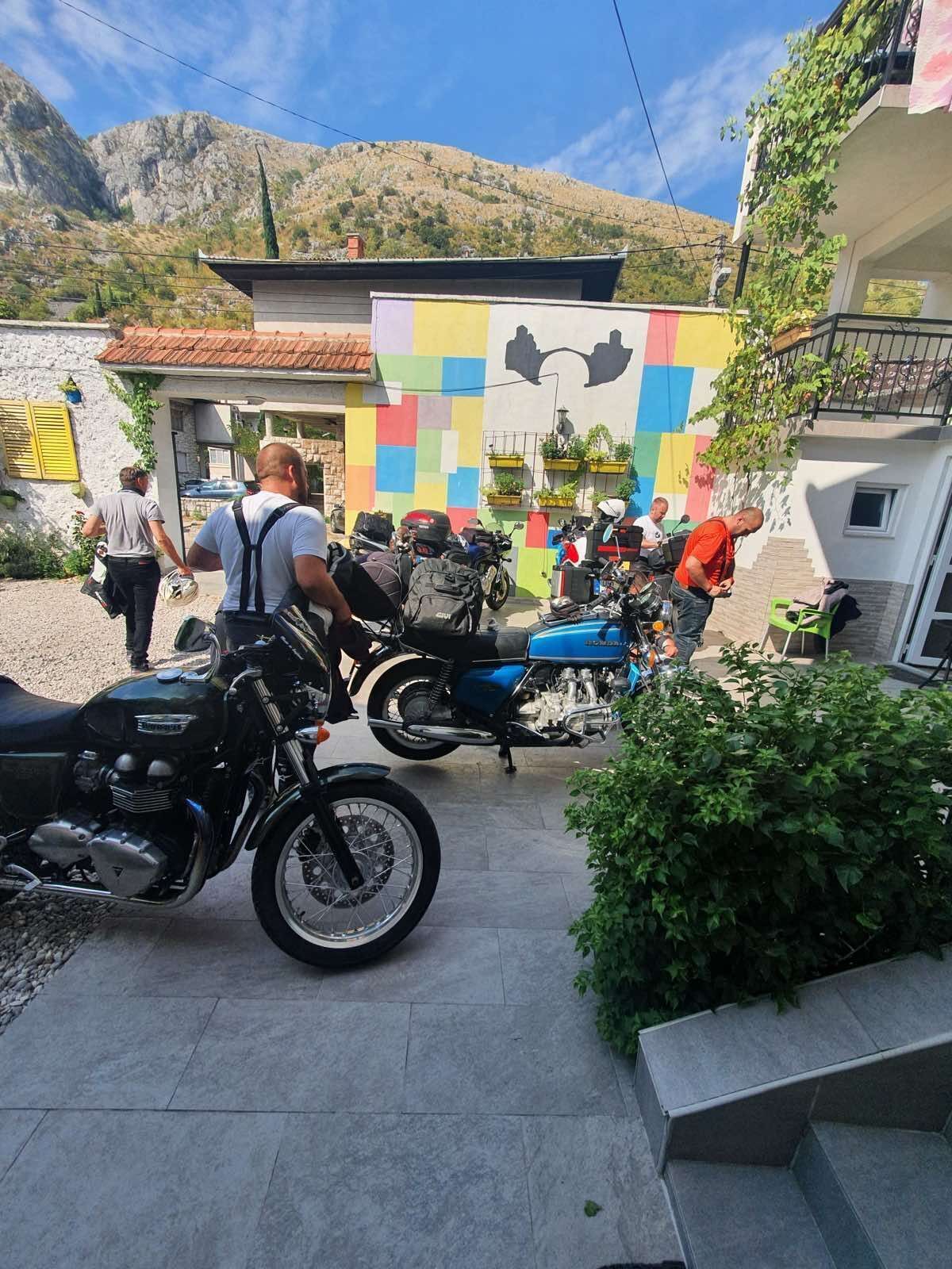 Pátio com motocicletas estacionadas, um mural colorido e montanhas ao fundo.