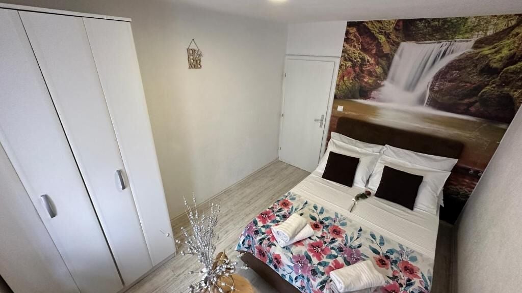 A bedroom with a bed, a wardrobe, a wall-mounted TV, and a decorative plant.
