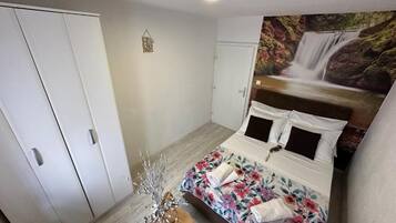A bedroom with a bed, a wardrobe, a wall-mounted TV, and a decorative plant.