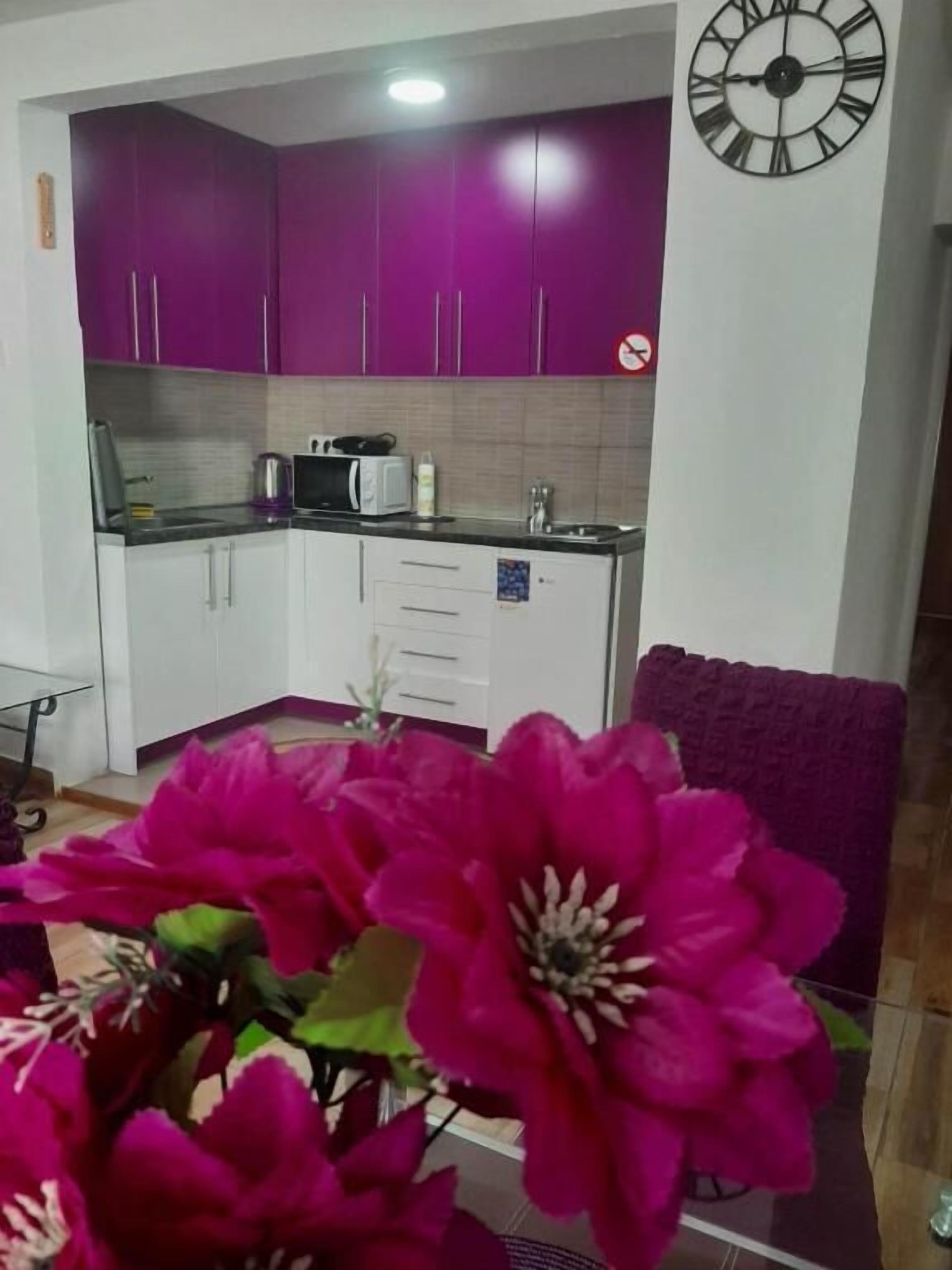 Une cuisine avec des meubles de couleur violette, une horloge et un arrangement floral.