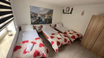 A hotel room with three beds, a wooden wardrobe, a painting of a cityscape, and a wall clock.
