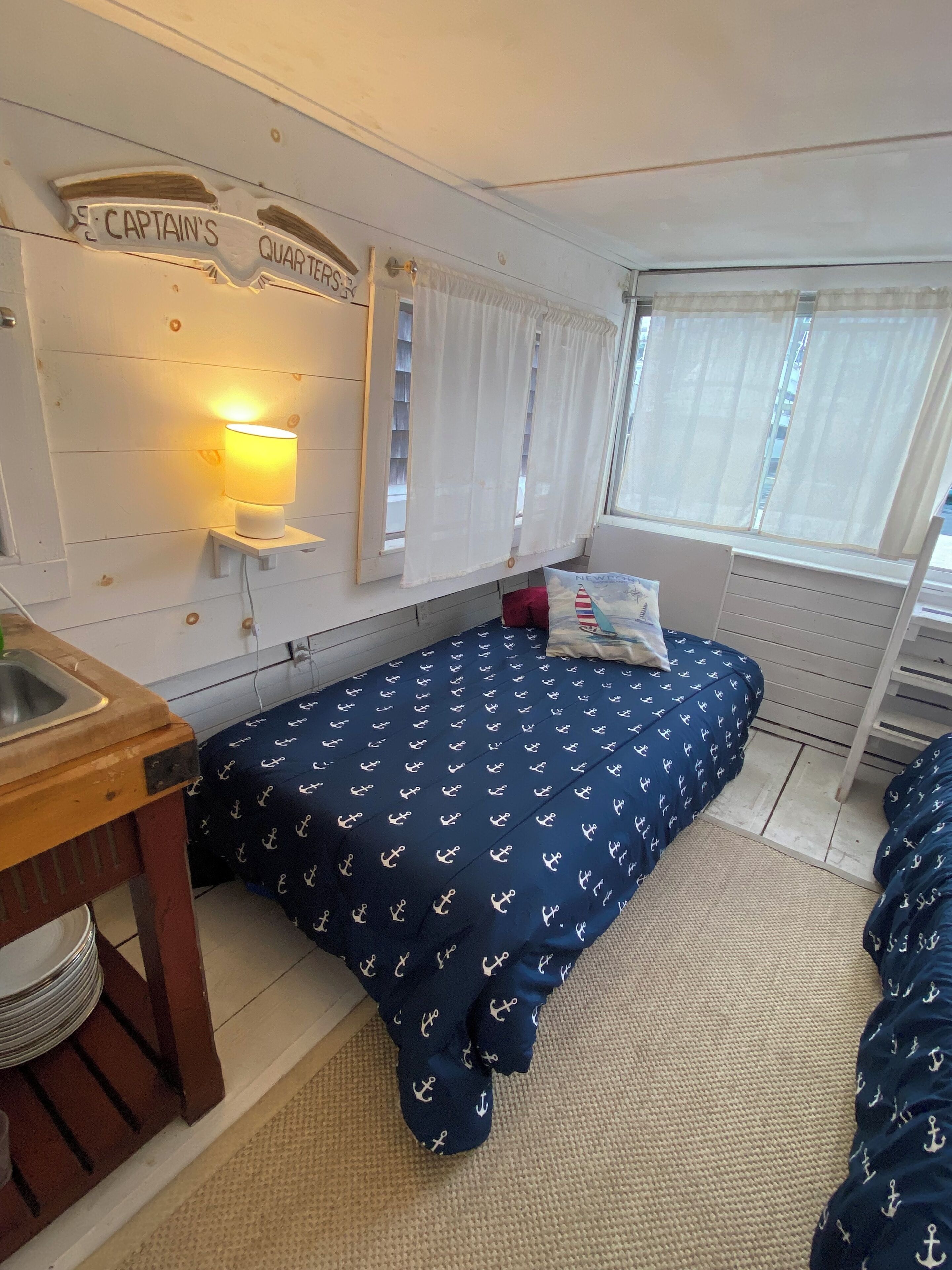 Una habitación pequeña con cama, una mesita y ventana con cortinas.