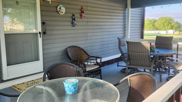 Een overdekte terras met rieten meubels, een glazen tafel en een deur met een deurmat.