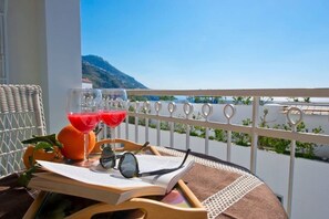 A balcony with a view of a body of water and a mountain, a wicker chair, a tray with drinks, glasses, and an open book. - La Coccinella House Praiano (Praiano)