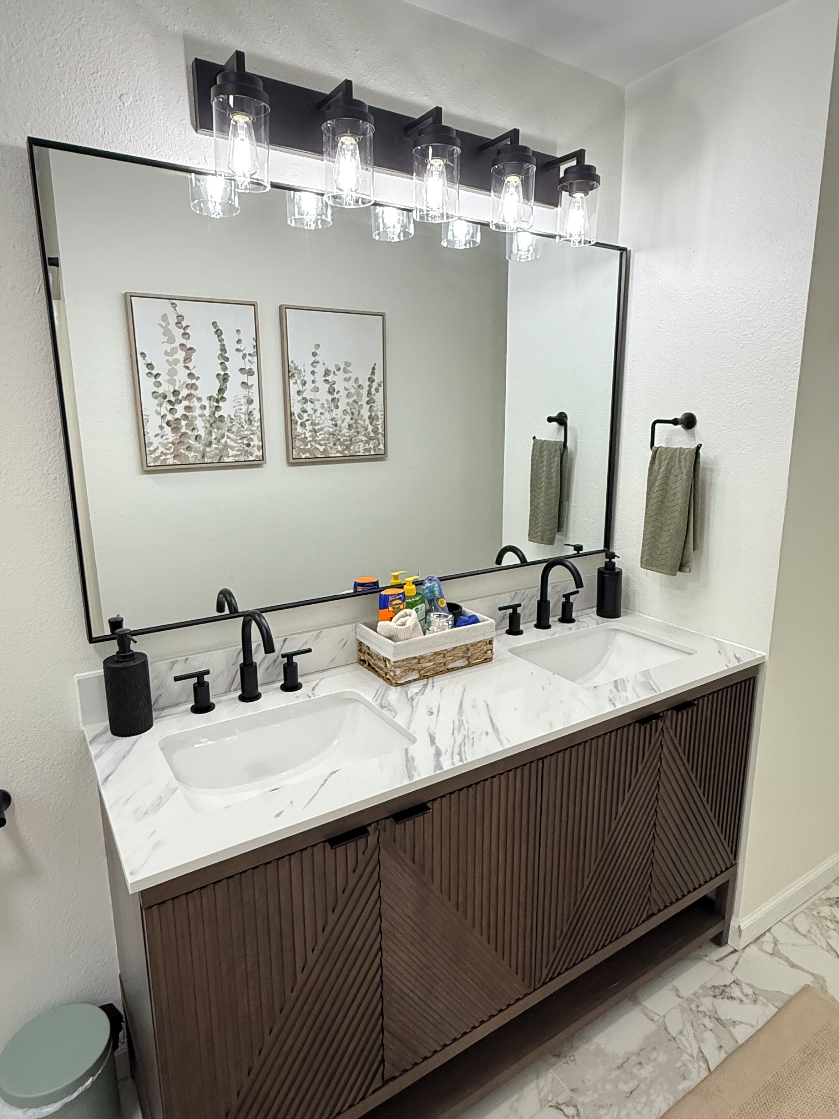 A bathroom with a double sink, a large mirror, and a light fixture above the mirror.