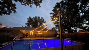 Ein Swimmingpool mit Lichterketten, einem Basketballkorb und einer überdachten Terrasse.