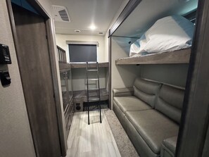 A compact room with a bunk bed, a small seating area, a ladder, and a window.