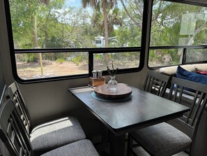 A dining area with a table and chairs, a window with a view of trees, and a vase with flowers on the table.