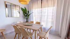 Un comedor con una mesa de madera, seis sillas, un espejo grande, una planta en maceta y cortinas de gasa.