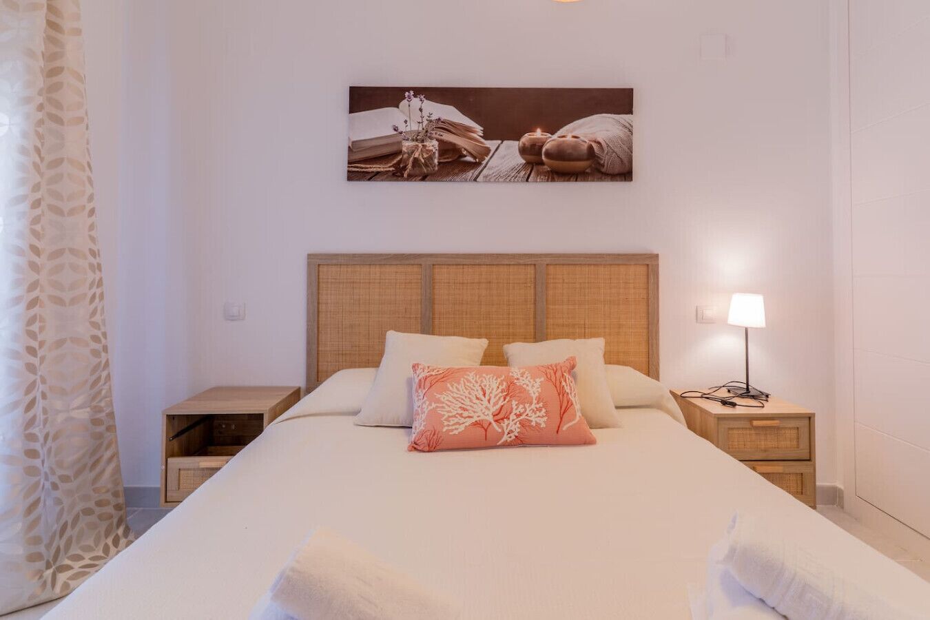 Habitación de hotel con una cama grande, dos mesitas de noche, una lámpara de pared y un cuadro enmarcado sobre la cama.