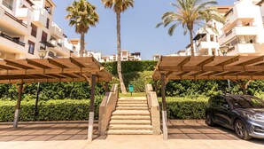 Zona residencial con una escalera que conduce a un edificio, rodeada de palmeras y un coche aparcado.