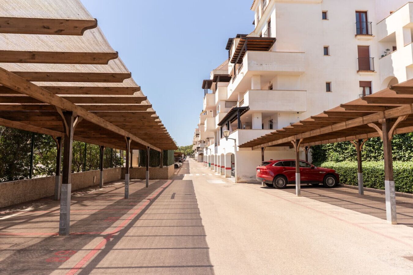 A row of modern apartment buildings with covered parking spaces and a red car parked in one.