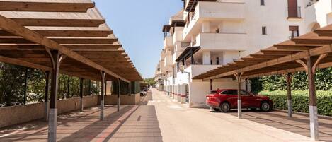 A row of modern apartment buildings with covered parking spaces and a red car parked in one.