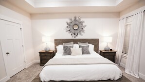 Un dormitorio con una cama grande, dos mesitas de noche, un espejo en la pared y una puerta.