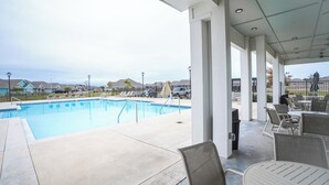 Un espacio al aire libre techado con piscina, sillones de descanso y mesas.