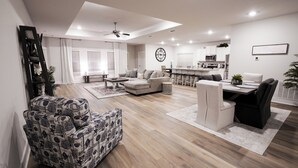 Una sala de estar moderna con un sofá, un sillón estampado, una mesa de comedor con sillas y una cocina al fondo.