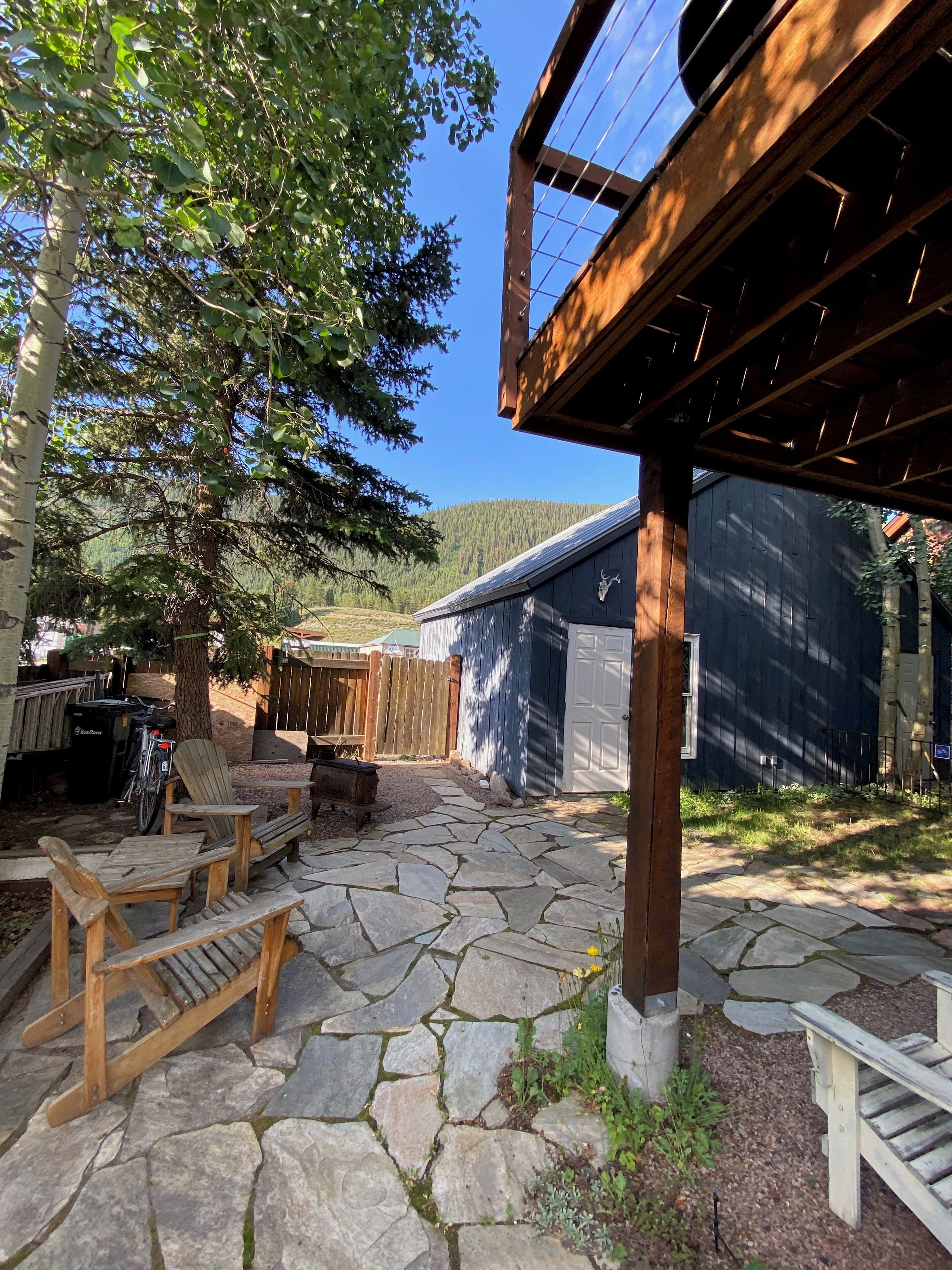 A stone patio with wooden furniture, a wooden pergola, and a garage.