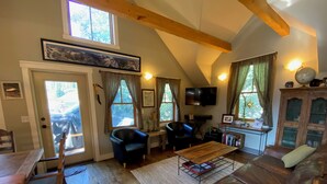 Ein gemütliches Wohnzimmer mit Holzbalkendecke, einem braunen Ledersofa, einem schwarzen Sessel, einem Couchtisch und einem an der Wand befestigten Fernseher.