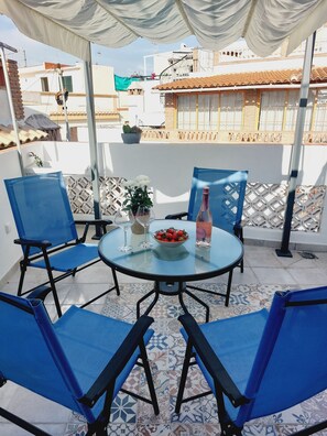 A round glass table with blue chairs, a bowl of strawberries, a bottle of water, and a glass of wine on a patio with patterned tiles. - Andalusian House with Sea View in the Old Town (Almuñécar)