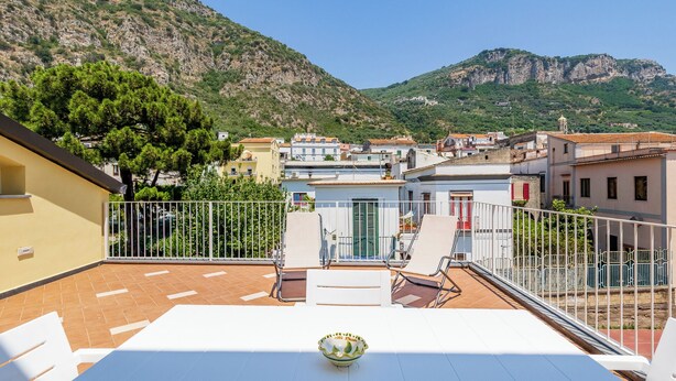 Eine Terrasse mit Tisch und Stühlen, mit Blick auf eine Stadt, Gebäude und Berge im Hintergrund.