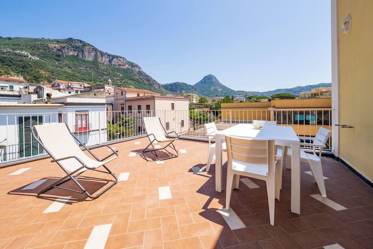 Una terraza con una mesa y sillas, una vista de la montaña y edificios al fondo.