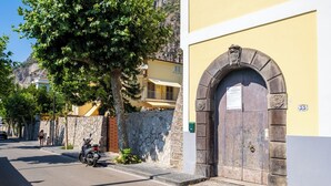 Eine Straße mit einer Steinmauer, einem abgestellten Roller und einem Gebäude mit einer Holztür und einem Schild.