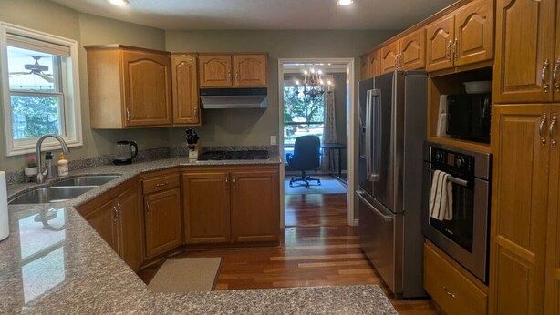 A kitchen with wooden cabinets, granite countertops, stainless steel appliances, and a view to a dining area.