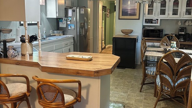 Una cocina con una isla central, taburetes de bar y sillas de mimbre.