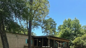 Una cabaña de madera con un porche, una pequeña terraza y un patio cubierto de césped.
