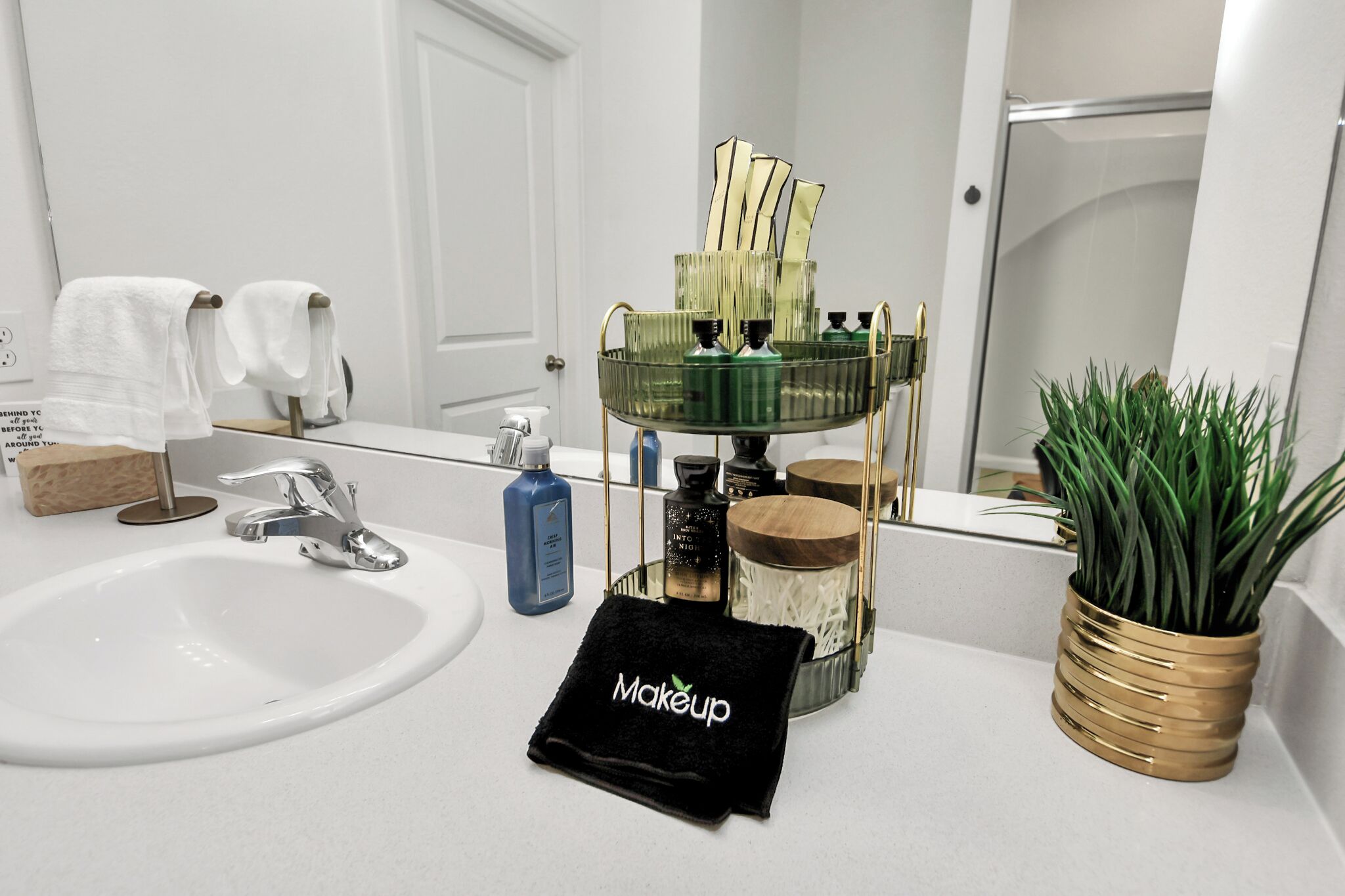 Une salle de bain avec un lavabo blanc, un miroir, un porte-serviettes, une plante verte et une trousse de maquillage.