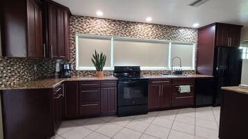 A kitchen with dark wooden cabinets, a tiled backsplash, a black stove, and a black refrigerator.