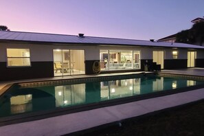 Une maison moderne dotée d’une piscine, de grandes fenêtres et d’un intérieur bien éclairé.