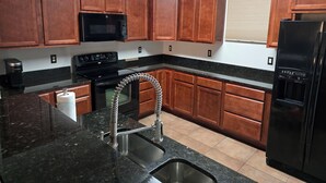 A kitchen with wooden cabinets, a black refrigerator, a stove, a microwave, and a sink with a flexible hose. - Executive Edge, Lakeside (Bean Station)