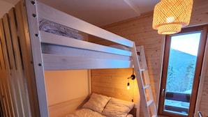 A bunk bed with a ladder, a small round table, a hanging light fixture, and a window with a view of trees and mountains.