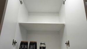 Un mobile bianco vuoto con due contenitori neri etichettati “ÁCÚCAR” e “CAFÉ” e un barattolo di chicchi di caffè.