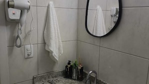 Bagno con lavabo su piano in granito, uno specchio, un asciugacapelli e un asciugamano appeso al muro.