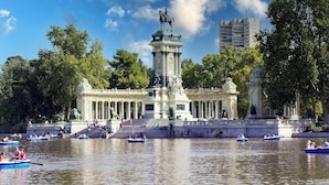 Een historisch monument met een centraal standbeeld, omgeven door een waterpartij met boten en mensen.