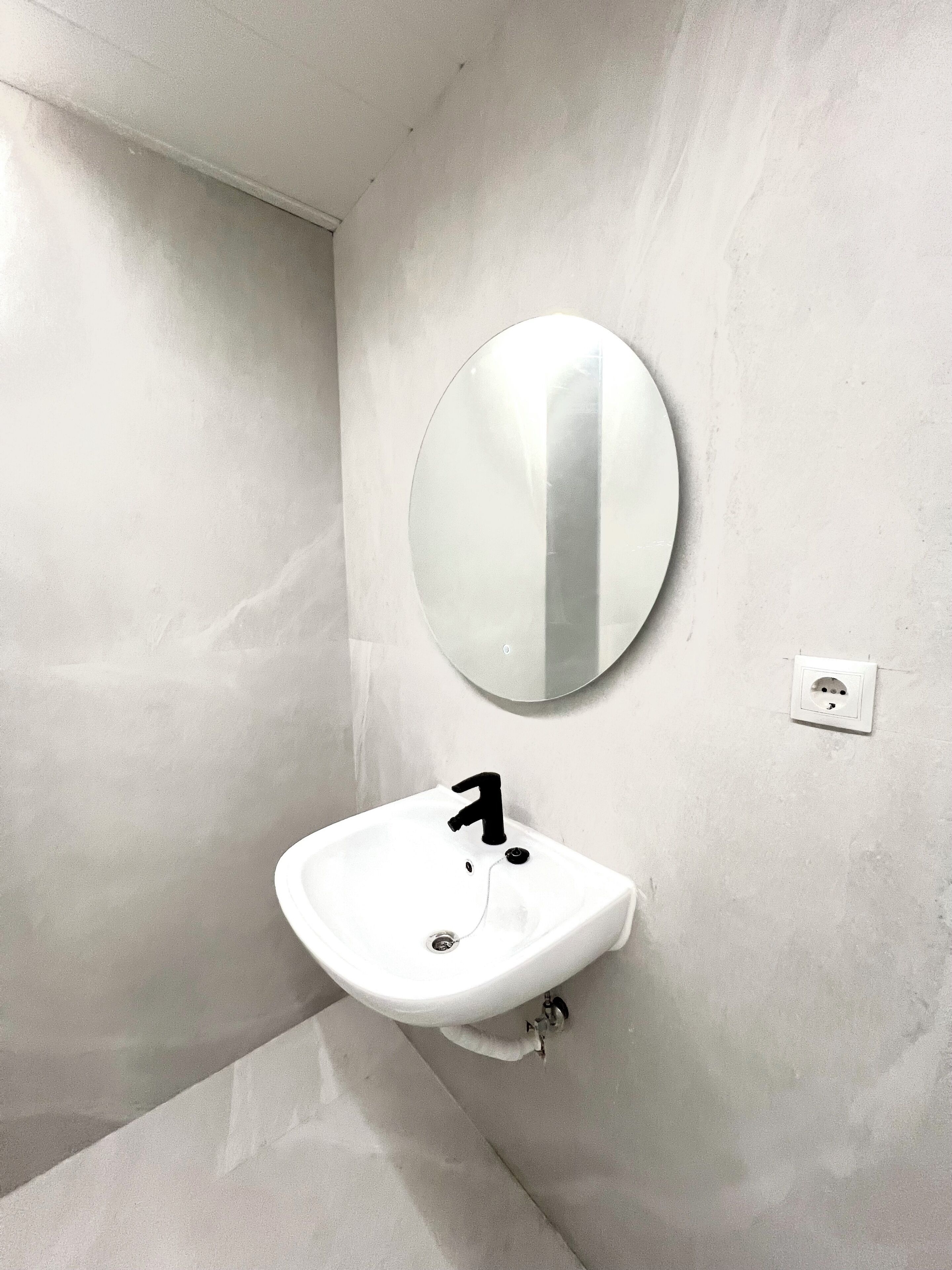 A bathroom with a white sink, a round mirror, and a wall-mounted light switch.