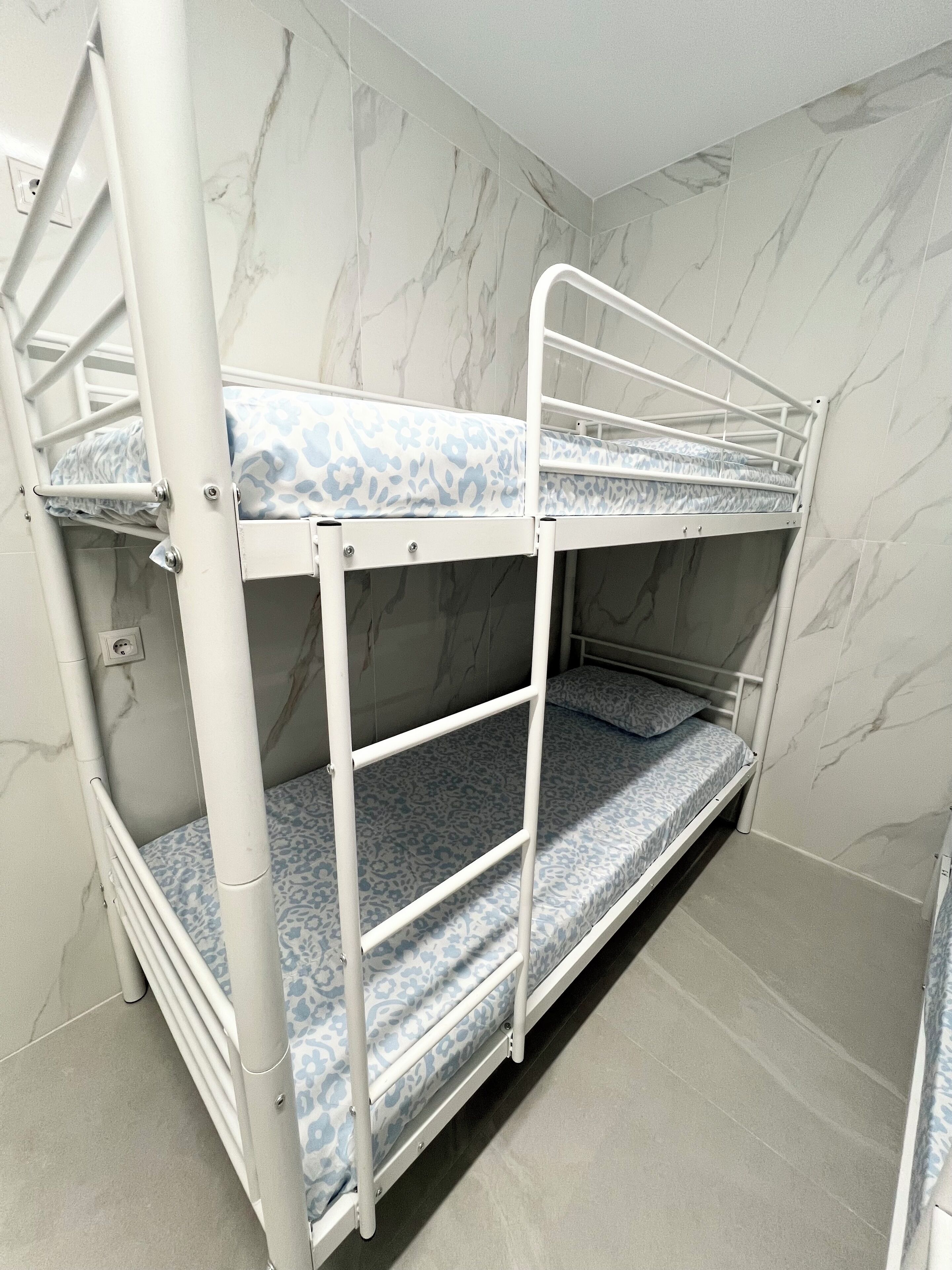 Un letto a castello con materasso decorato, struttura in metallo bianco e pareti con motivo marmorizzato.