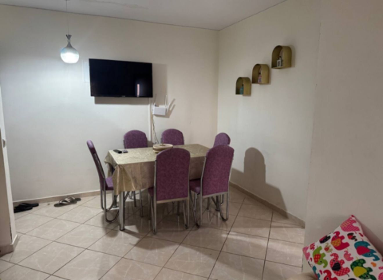 A dining area with a table and chairs, a flat-screen TV mounted on the wall, and a small table with decorative items.