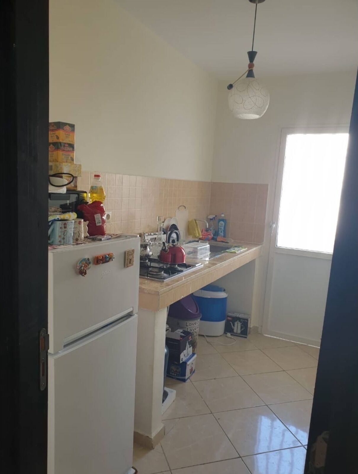 A compact kitchen with a refrigerator, stove, and a hanging light fixture.
