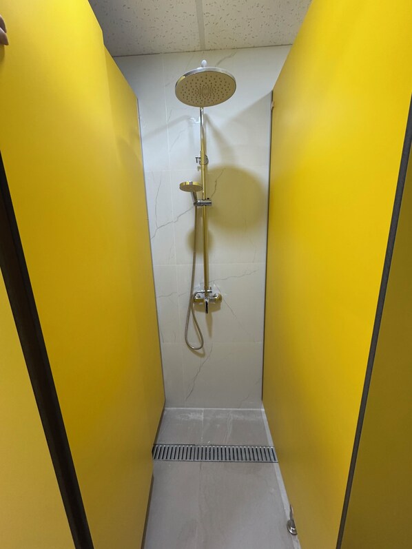 A narrow shower stall with yellow walls and a white tiled floor. - Hostel Vallecas (Madrid)