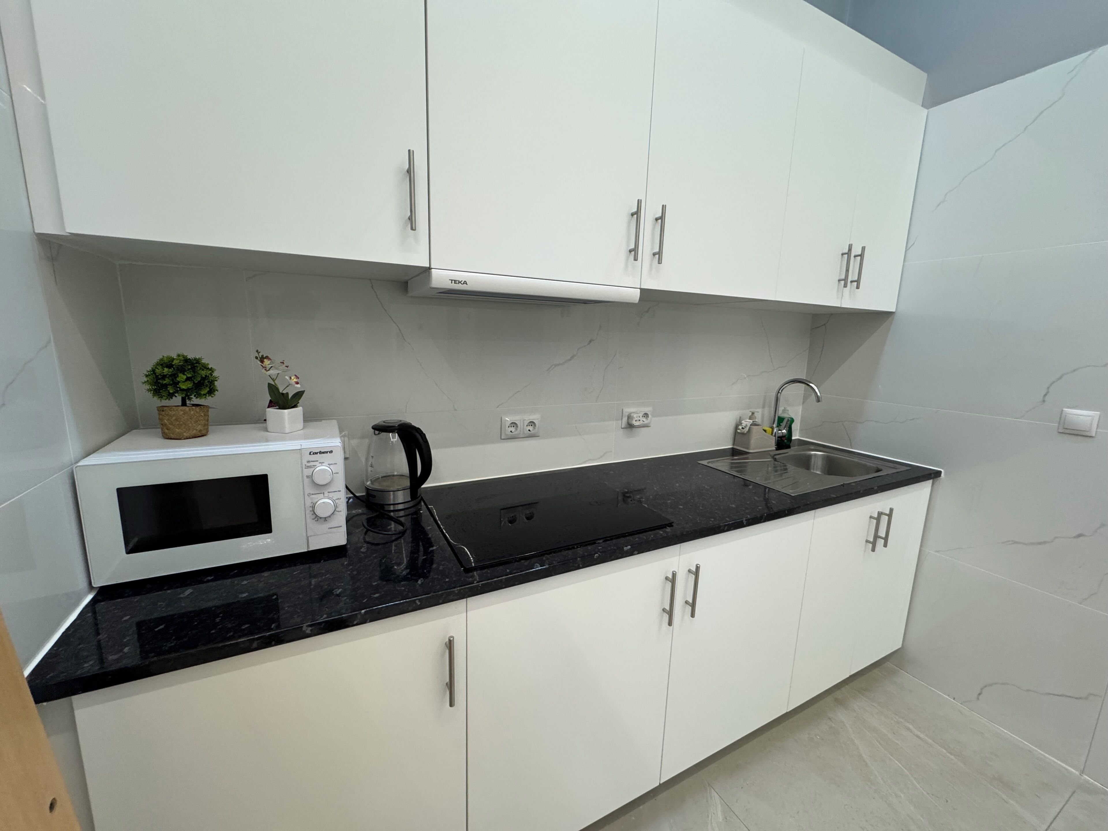 Een moderne keuken met witte kastjes, een zwart aanrecht, een magnetron, een koffiezetapparaat en een spoelbak.