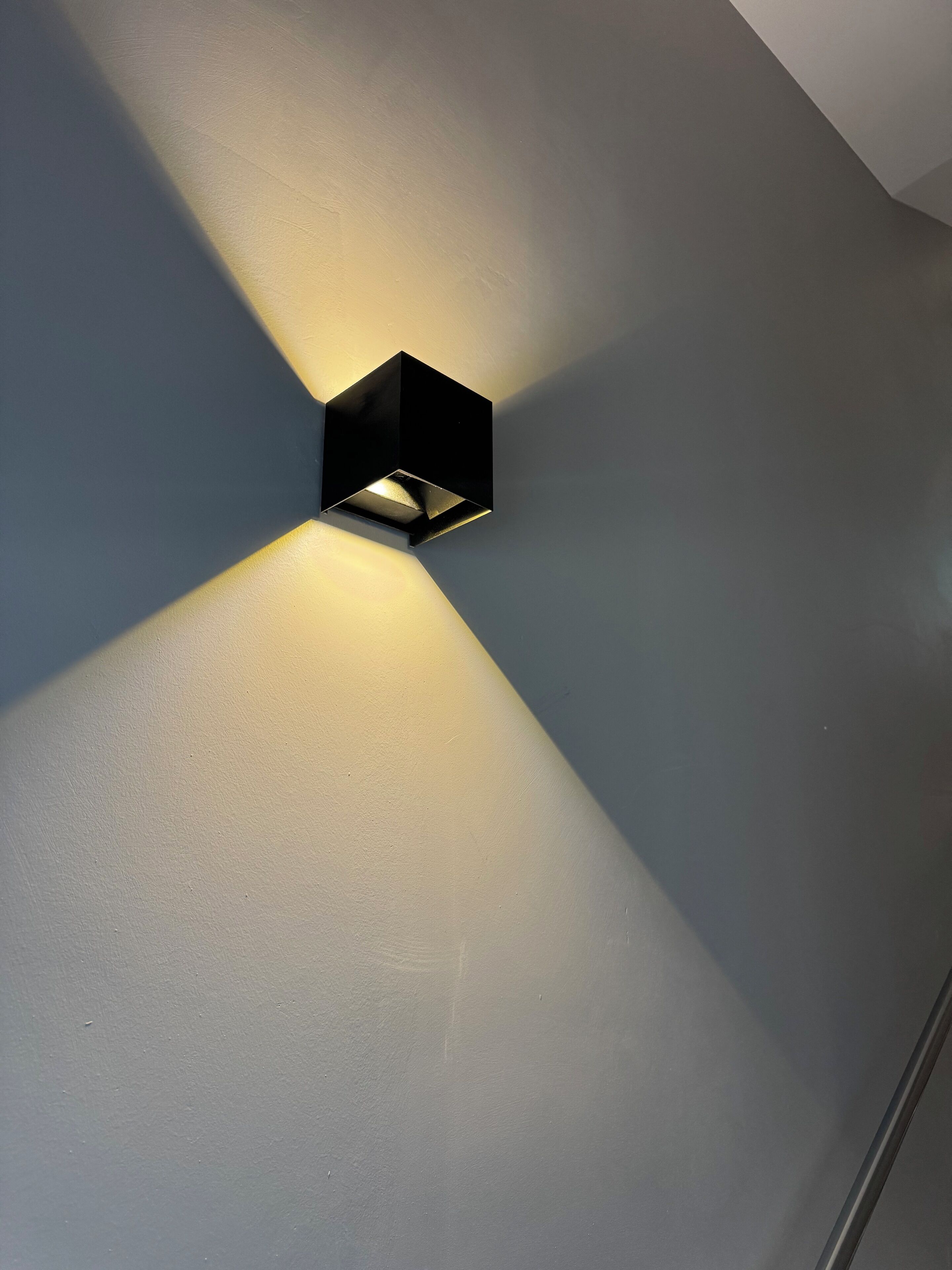A modern, minimalist wall-mounted light fixture with a geometric design.